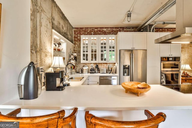 kitchen with brick wall, appliances with stainless steel finishes, a kitchen bar, and white cabinetry