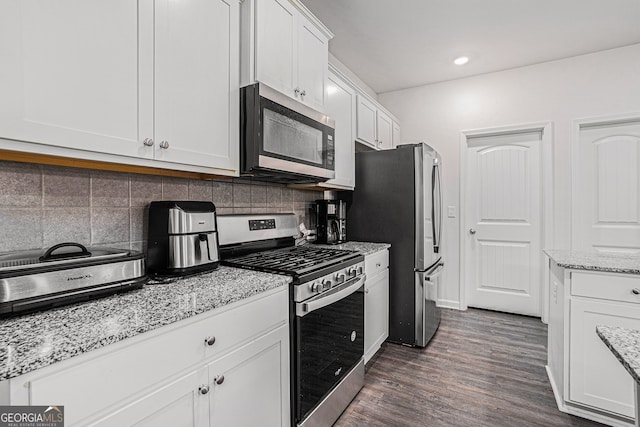 kitchen with stainless steel appliances, dark hardwood / wood-style flooring, tasteful backsplash, light stone countertops, and white cabinetry