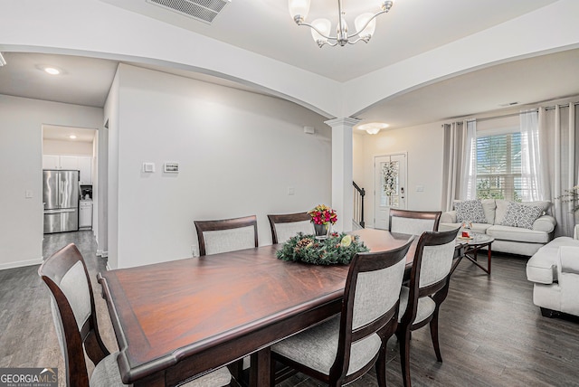 dining area featuring dark wood-type flooring, a notable chandelier, and decorative columns