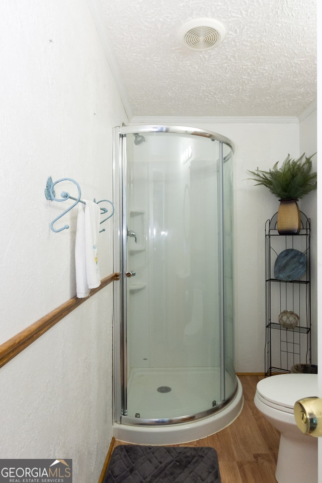 bathroom featuring a shower with door, toilet, hardwood / wood-style flooring, and a textured ceiling