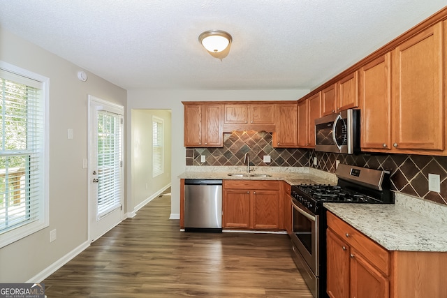 kitchen with appliances with stainless steel finishes, sink, a textured ceiling, light stone counters, and dark hardwood / wood-style floors