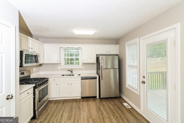 kitchen featuring light hardwood / wood-style flooring, stainless steel appliances, sink, white cabinets, and a textured ceiling