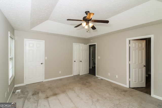 unfurnished bedroom with a textured ceiling, light colored carpet, a tray ceiling, and ceiling fan