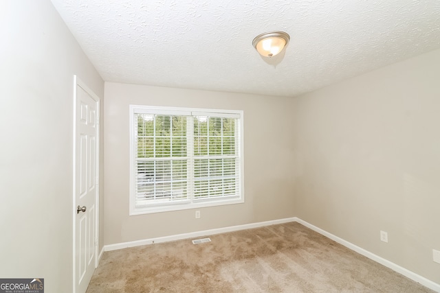 spare room featuring a textured ceiling and light colored carpet