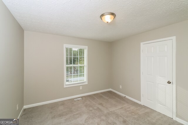 empty room with a textured ceiling and light colored carpet