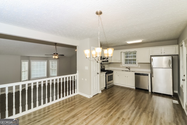 kitchen featuring hardwood / wood-style flooring, white cabinets, pendant lighting, appliances with stainless steel finishes, and ceiling fan with notable chandelier