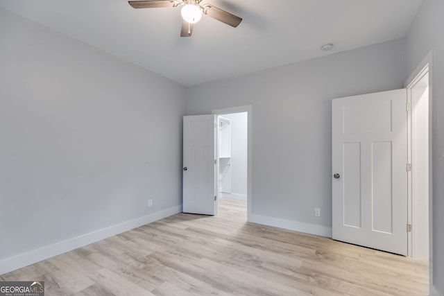 unfurnished bedroom with ceiling fan, light hardwood / wood-style floors, a walk in closet, and a closet