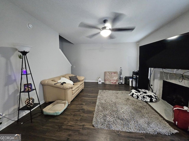 living room with ceiling fan, a stone fireplace, a textured ceiling, and dark hardwood / wood-style flooring