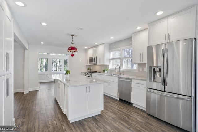 kitchen featuring light stone counters, stainless steel appliances, sink, white cabinetry, and hanging light fixtures