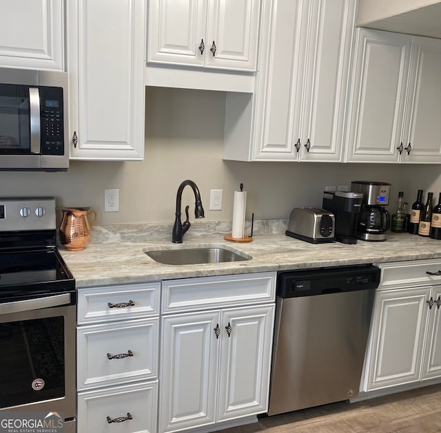 kitchen featuring light stone countertops, appliances with stainless steel finishes, light wood-type flooring, sink, and white cabinetry