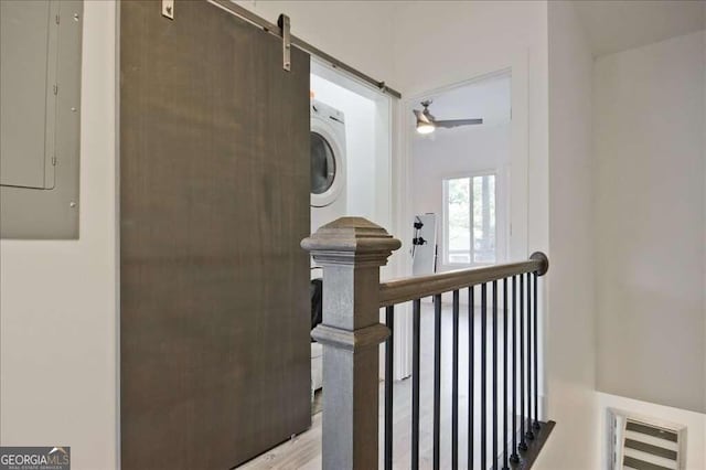 interior space with hardwood / wood-style floors, electric panel, stacked washer / dryer, and a barn door