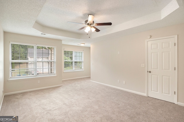 carpeted spare room featuring a textured ceiling, ceiling fan, and a raised ceiling