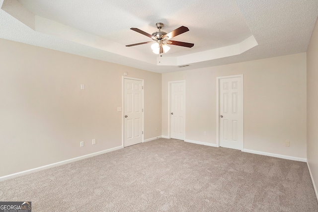 unfurnished bedroom with ceiling fan, carpet flooring, a textured ceiling, and a tray ceiling