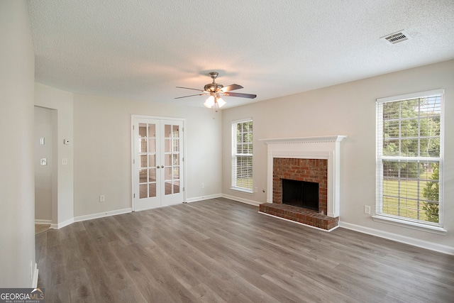 unfurnished living room featuring french doors, a brick fireplace, a textured ceiling, and dark hardwood / wood-style flooring