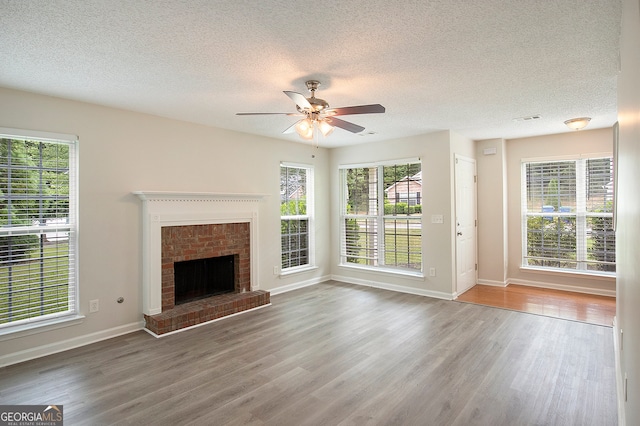 unfurnished living room with ceiling fan, a textured ceiling, a brick fireplace, and hardwood / wood-style floors