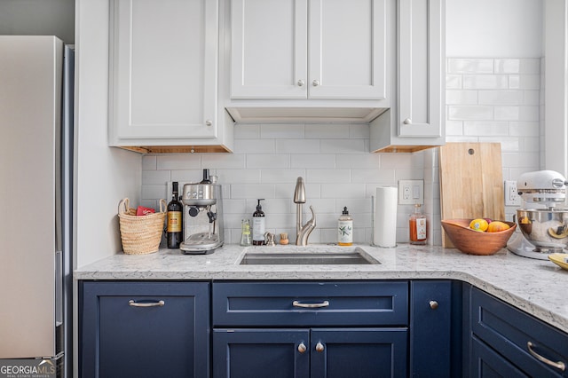 kitchen featuring backsplash, stainless steel fridge, sink, blue cabinetry, and white cabinetry