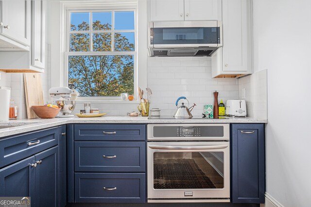 kitchen featuring stainless steel appliances, light stone countertops, blue cabinetry, white cabinetry, and tasteful backsplash