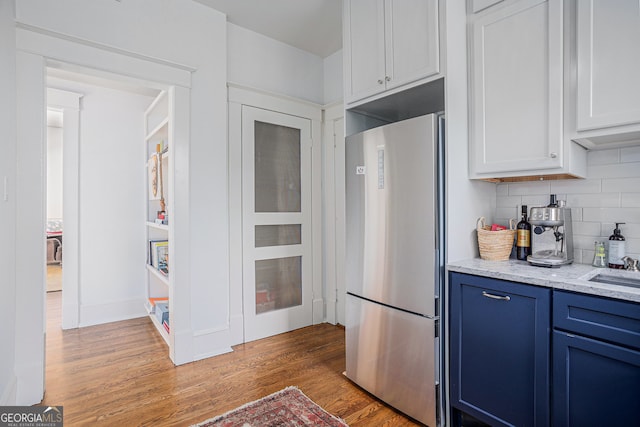 kitchen featuring tasteful backsplash, light stone countertops, wood-type flooring, blue cabinets, and stainless steel fridge