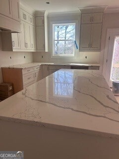 kitchen with custom exhaust hood, ornamental molding, light stone counters, and a center island