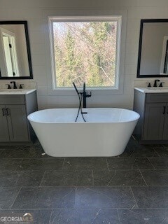 full bathroom with stone finish floor, two vanities, a sink, and a freestanding bath