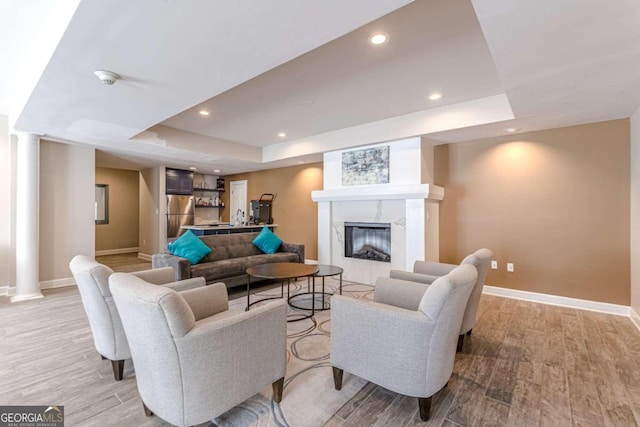 living room with a high end fireplace, light wood-type flooring, and a raised ceiling