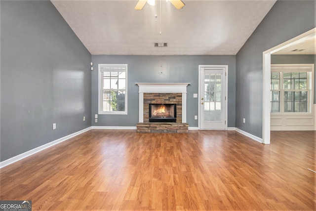 unfurnished living room featuring ceiling fan, a stone fireplace, light hardwood / wood-style flooring, and vaulted ceiling