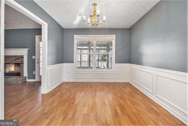 unfurnished dining area with a stone fireplace, light wood-type flooring, a chandelier, and a textured ceiling