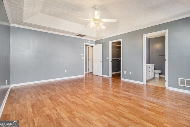 unfurnished bedroom featuring a walk in closet, ornamental molding, connected bathroom, light wood-type flooring, and a textured ceiling