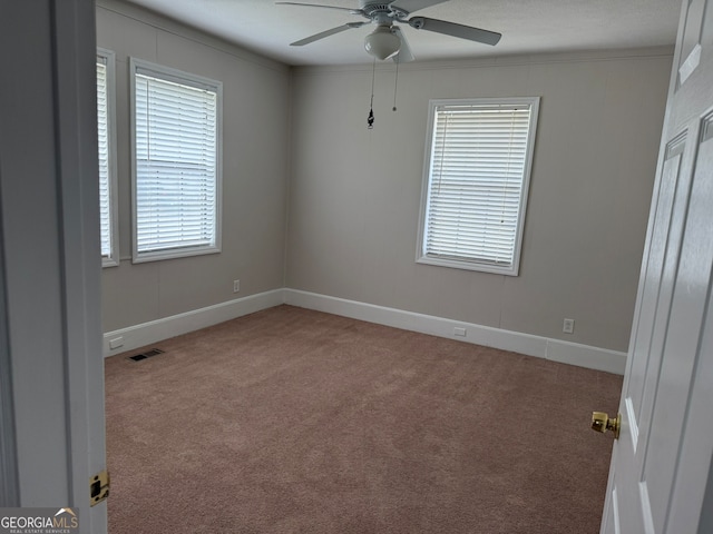 carpeted empty room with ceiling fan, ornamental molding, and a wealth of natural light