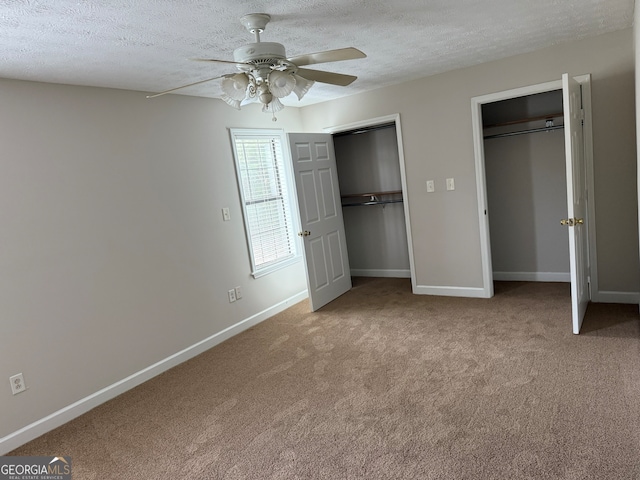 unfurnished bedroom featuring ceiling fan, light carpet, a textured ceiling, and two closets