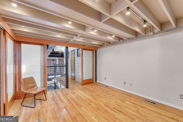 basement featuring rail lighting and light hardwood / wood-style flooring