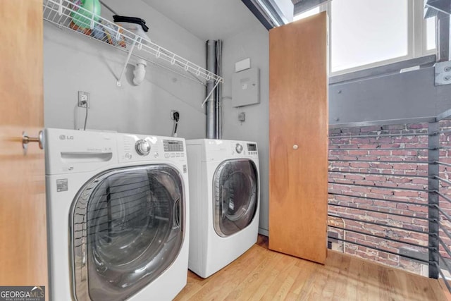 clothes washing area featuring brick wall, light hardwood / wood-style flooring, and washer and dryer