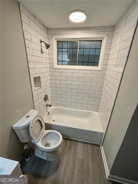 bathroom featuring a textured ceiling, tiled shower / bath combo, wood-type flooring, and toilet