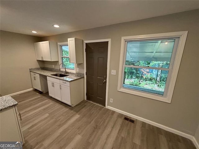 kitchen featuring light hardwood / wood-style floors, sink, light stone counters, and white cabinets