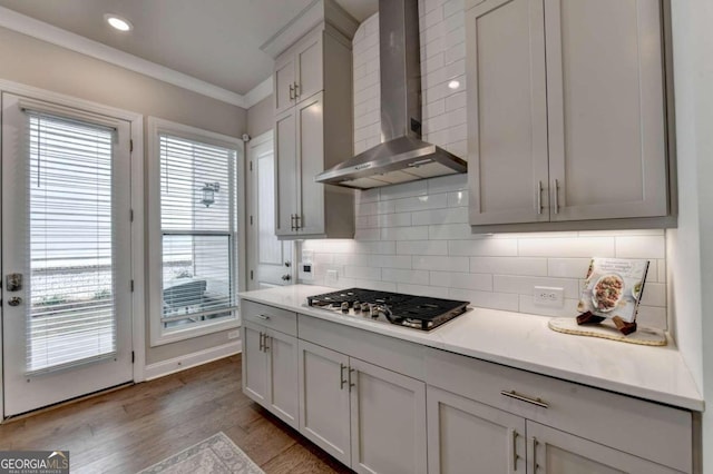 kitchen with wall chimney range hood, stainless steel gas stovetop, light countertops, backsplash, and ornamental molding