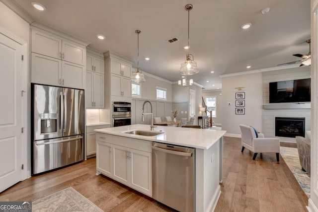 kitchen featuring stainless steel appliances, visible vents, ornamental molding, a sink, and open floor plan