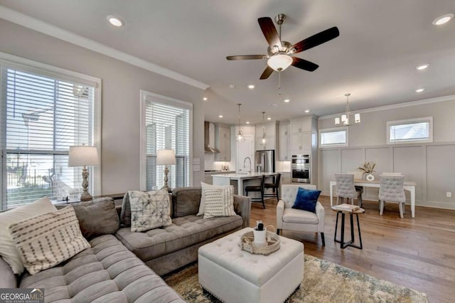 living room with light wood finished floors, ceiling fan, and ornamental molding