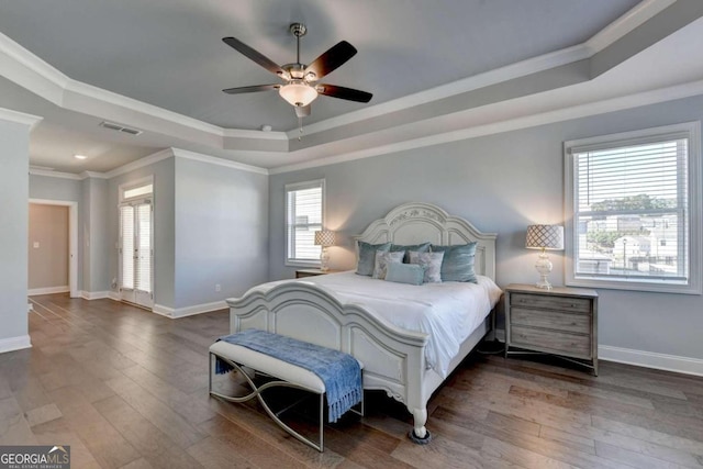 bedroom with wood finished floors, visible vents, a raised ceiling, and multiple windows