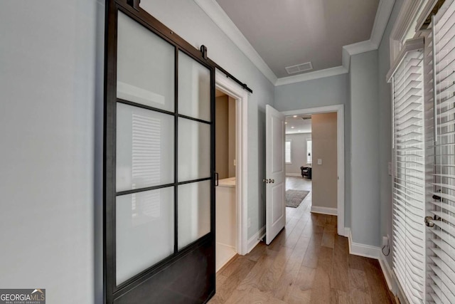 hallway featuring a barn door, visible vents, ornamental molding, light wood-type flooring, and baseboards