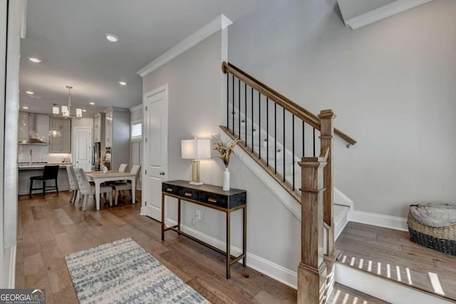 staircase featuring crown molding, a chandelier, wood-type flooring, and sink