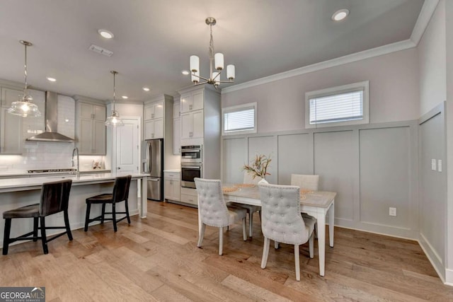 dining space with a decorative wall, crown molding, an inviting chandelier, light wood-style flooring, and visible vents