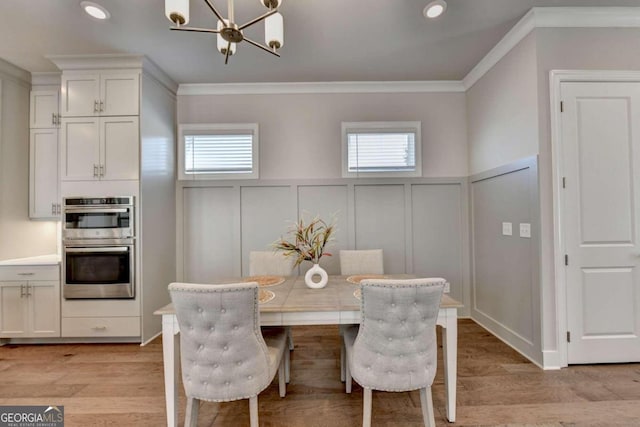 dining area with a notable chandelier, a decorative wall, a wealth of natural light, and ornamental molding