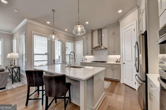 kitchen with wall chimney range hood, a sink, stainless steel appliances, light wood-style flooring, and ornamental molding
