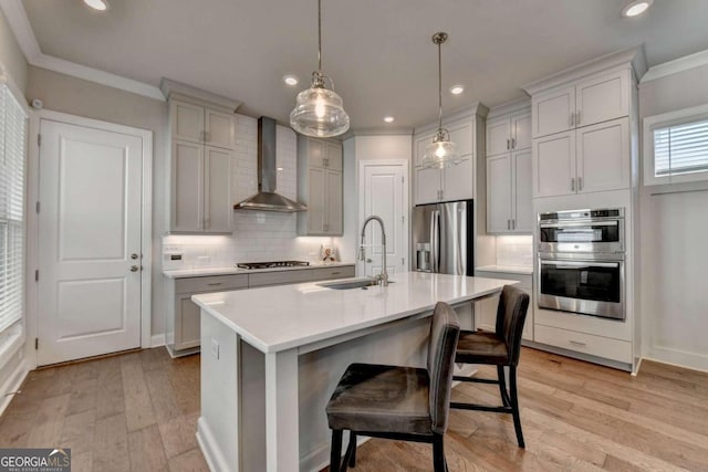 kitchen featuring wall chimney exhaust hood, sink, a kitchen bar, pendant lighting, and appliances with stainless steel finishes