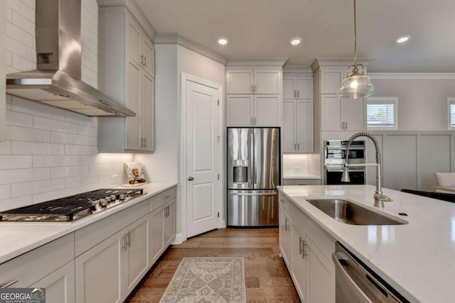 kitchen with appliances with stainless steel finishes, white cabinets, wall chimney range hood, and pendant lighting