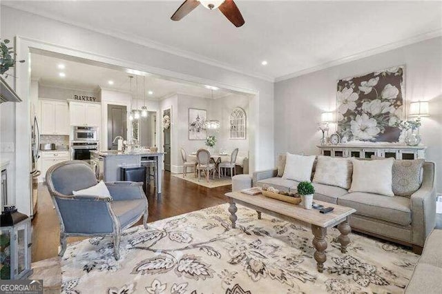 living room featuring ceiling fan, light wood-type flooring, ornamental molding, and sink