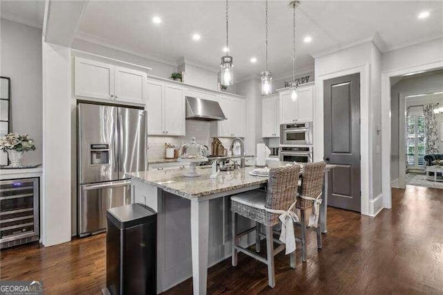 kitchen with wall chimney exhaust hood, white cabinets, an island with sink, and appliances with stainless steel finishes