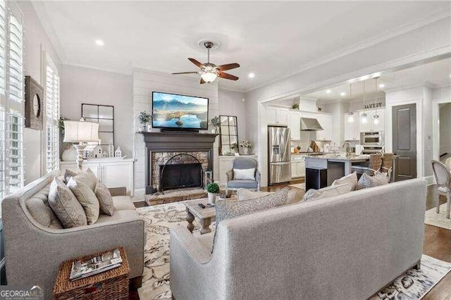 living room featuring a fireplace, wood-type flooring, ceiling fan, and ornamental molding