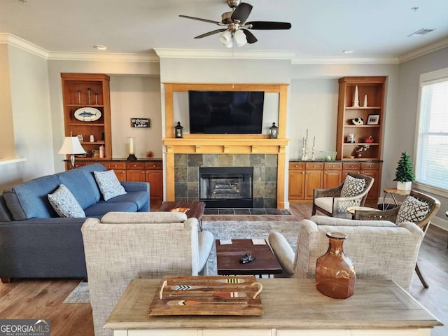 living room with ceiling fan, crown molding, light wood-type flooring, and a tile fireplace