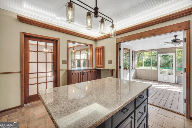 kitchen featuring ceiling fan, crown molding, light stone countertops, and hanging light fixtures